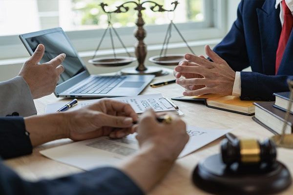 A group of lawyers are sitting at a table with a laptop and scales of justice.