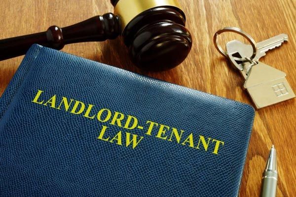 A blue book titled landlord-tenant law is on a wooden table next to a gavel and keys.