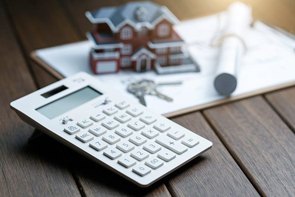 A calculator is sitting on a wooden table next to a model house and keys.