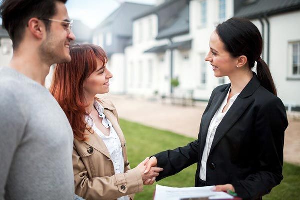 A woman is shaking hands with a man and woman in front of a house.