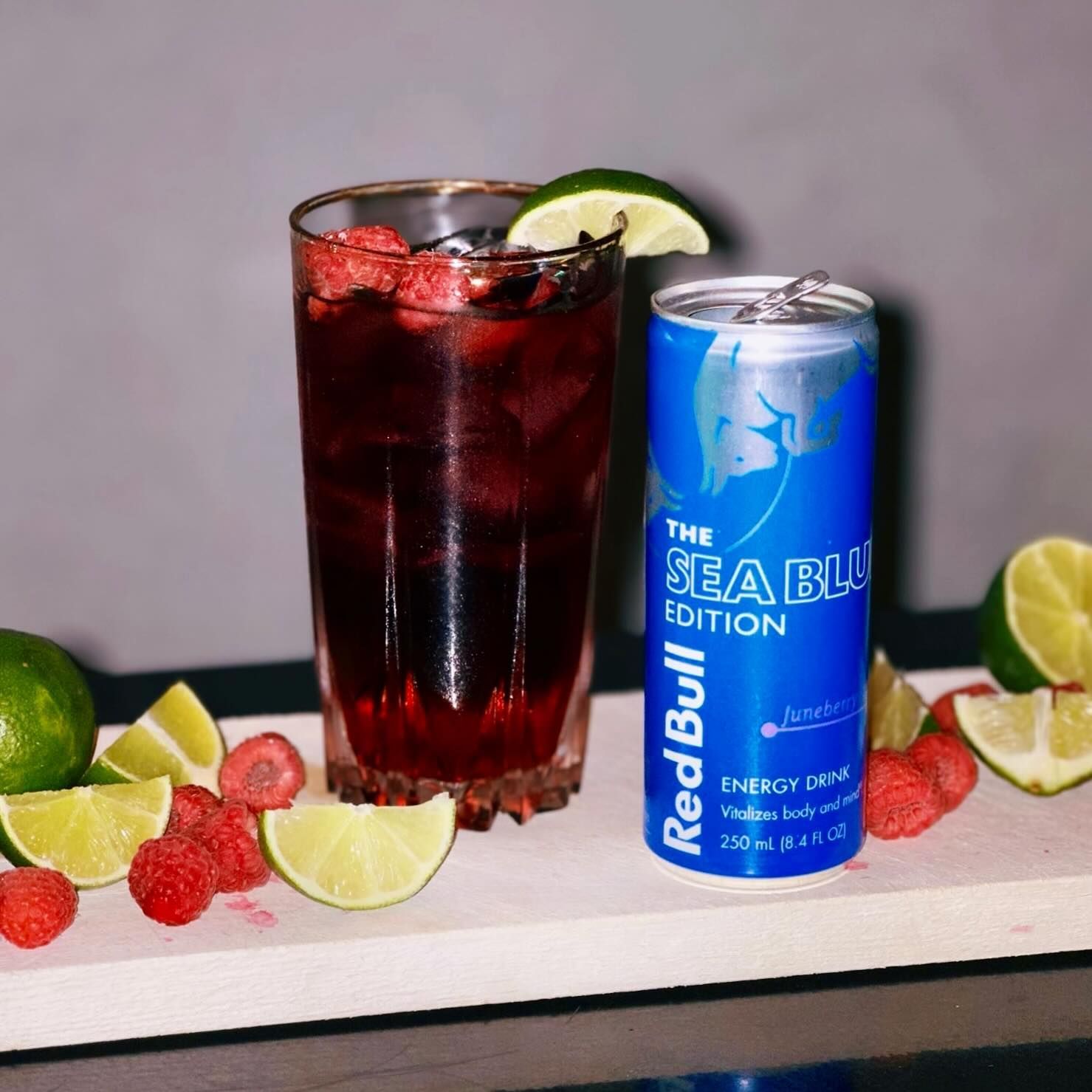 A glass of a red drink with raspberries and lime, next to a can of 