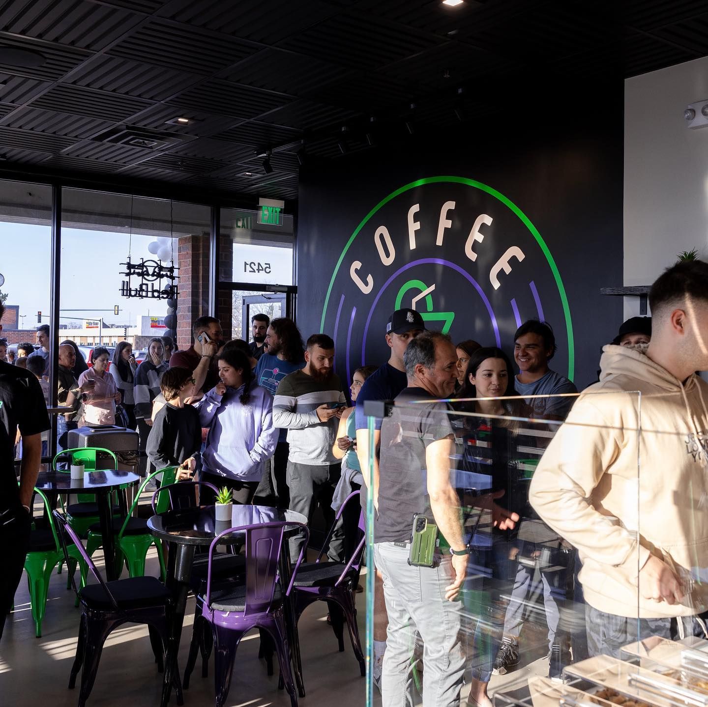 People line up inside a coffee shop with a neon 