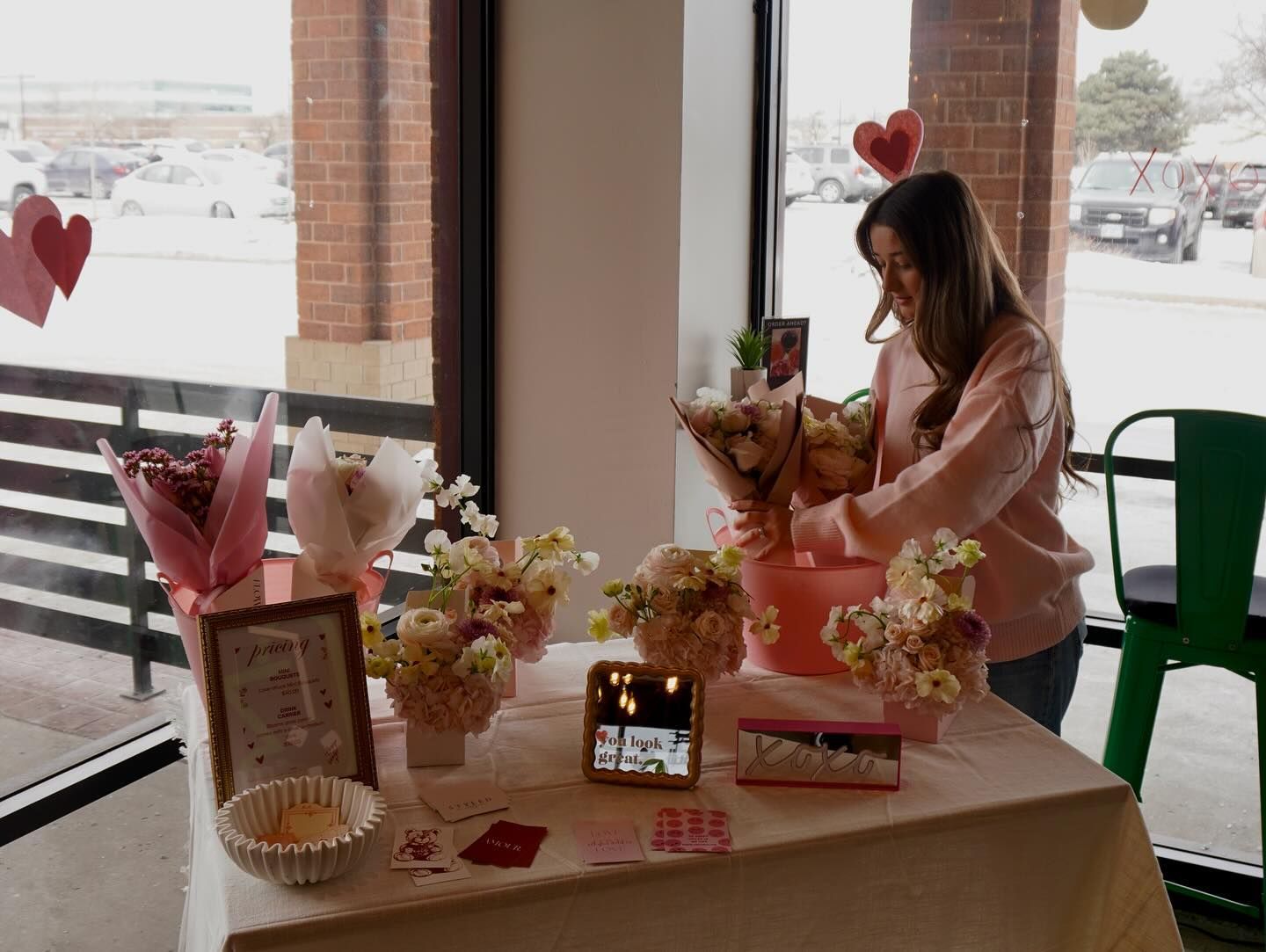 Woman arranging flowers on a table in front of a window. Pink and white flowers, Valentine's Day decorations.