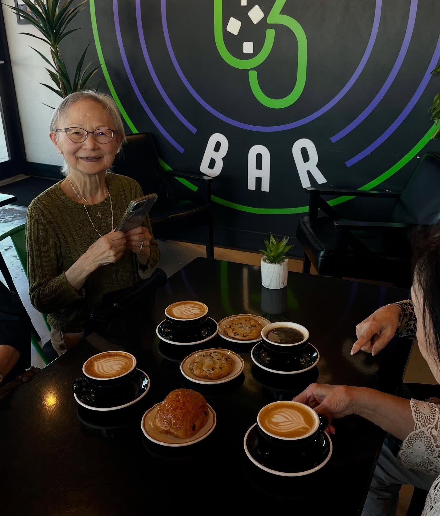 Woman at table in coffee shop with lattes and cookies. 