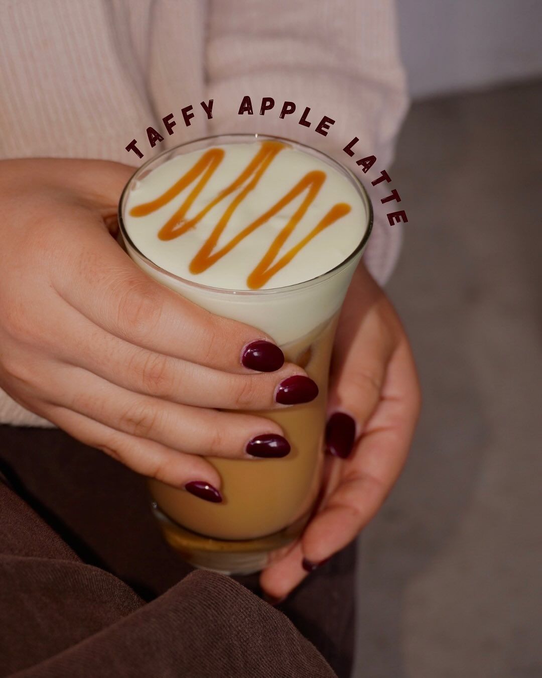 Person holding a tall glass of a Taffy Apple Latte, caramel drizzle on top.