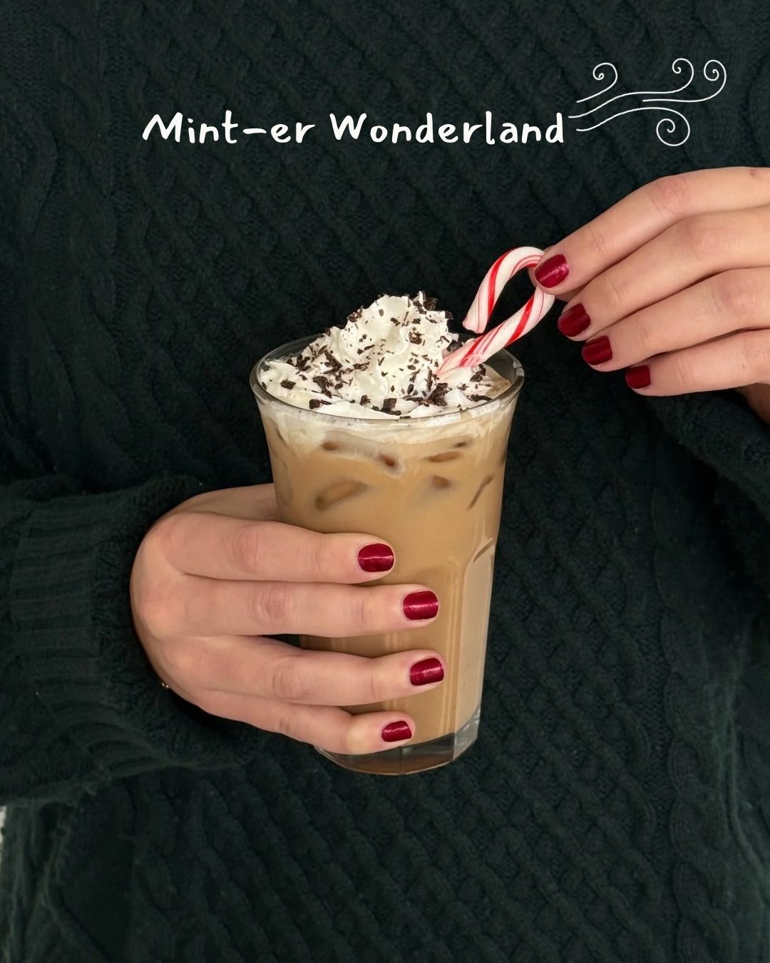 Person holding an iced coffee drink topped with whipped cream and a candy cane.