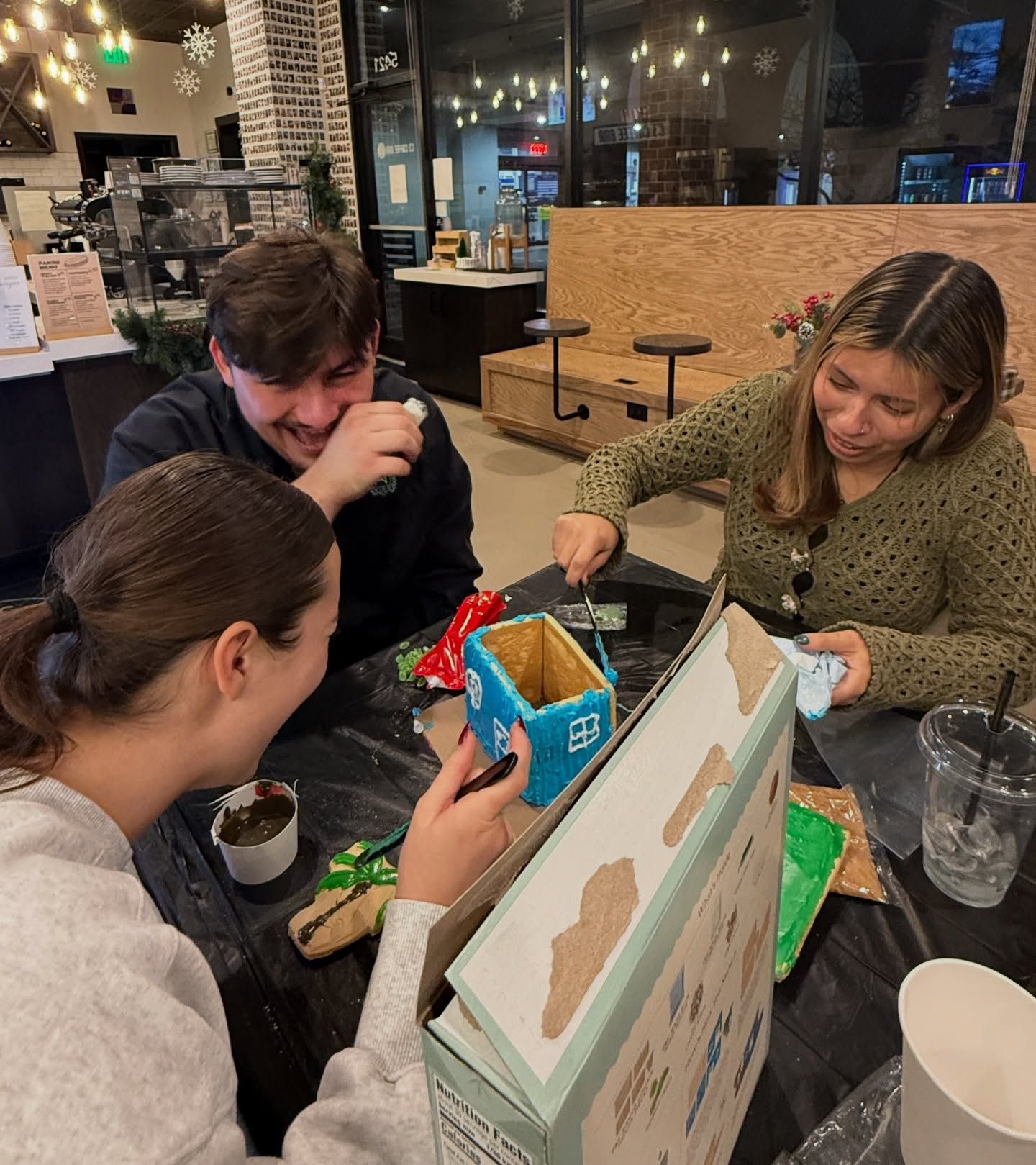 Three people painting small objects at a table. One laughs, while two others work, surrounded by craft supplies.