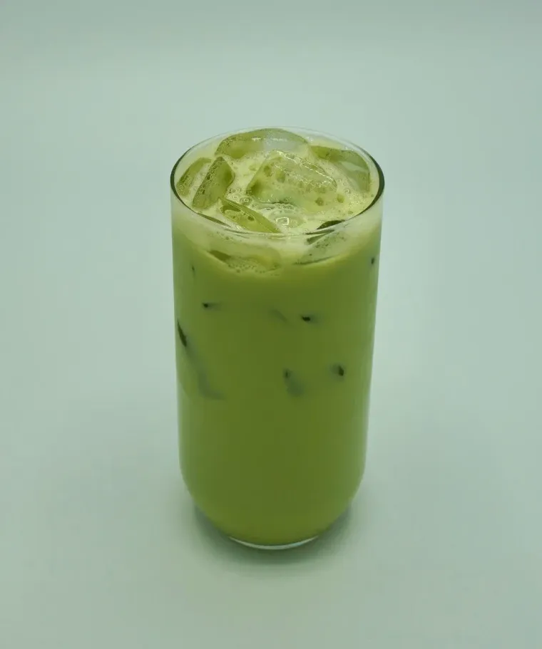 Iced matcha latte in a tall glass, pale green with ice cubes, on a light green background.
