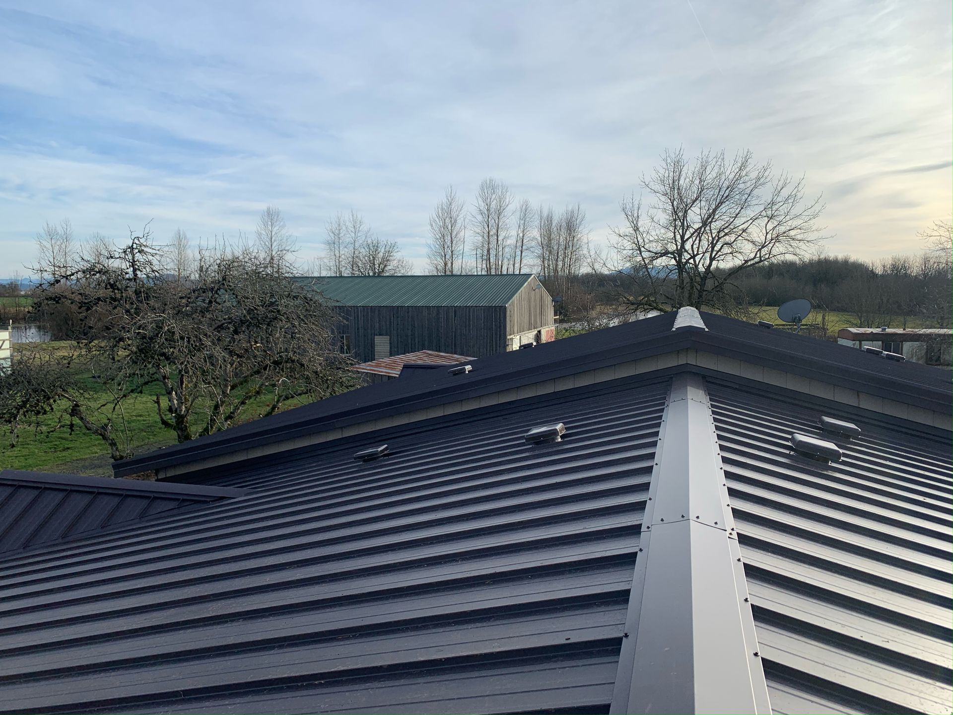 A black roof with a green building in the background.