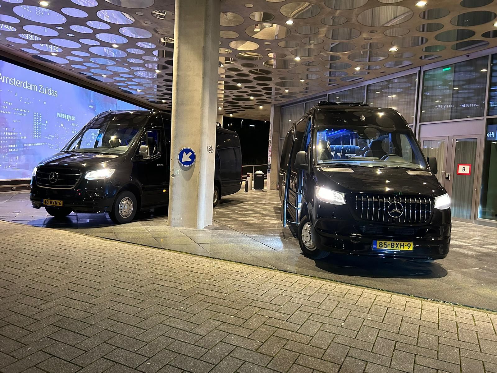Voor een gebouw staan twee zwarte taxi busjes van taxi amstelveen geparkeerd.