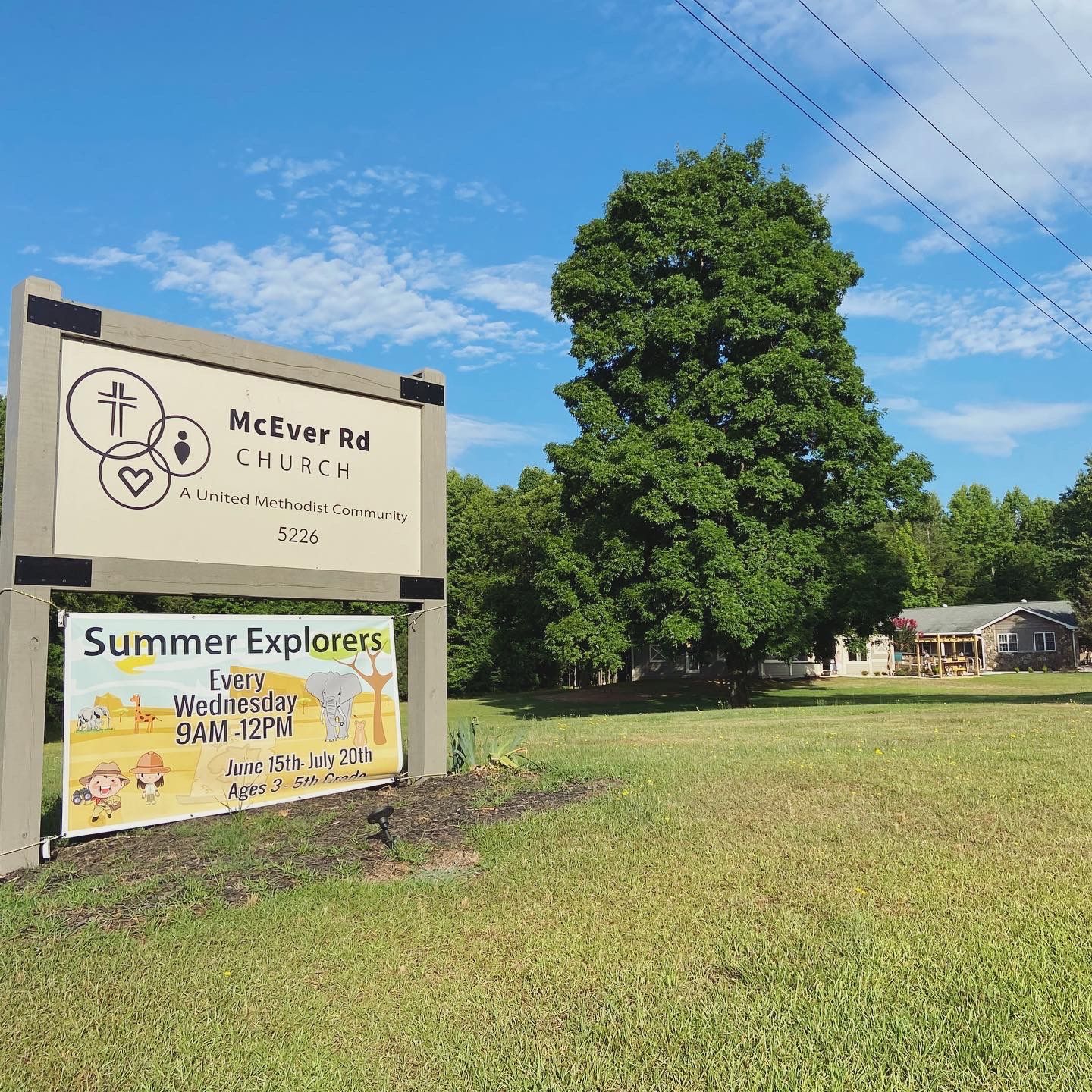 A sign for a church is sitting in the middle of a grassy field.