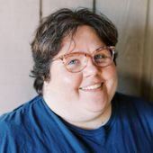 A woman wearing glasses and a blue shirt is smiling for the camera.