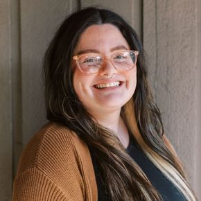 A woman wearing glasses and a brown sweater is smiling for the camera.