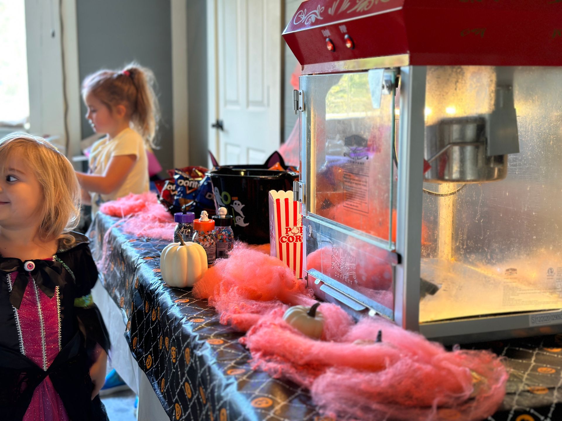 Two little girls are standing in front of a popcorn machine.