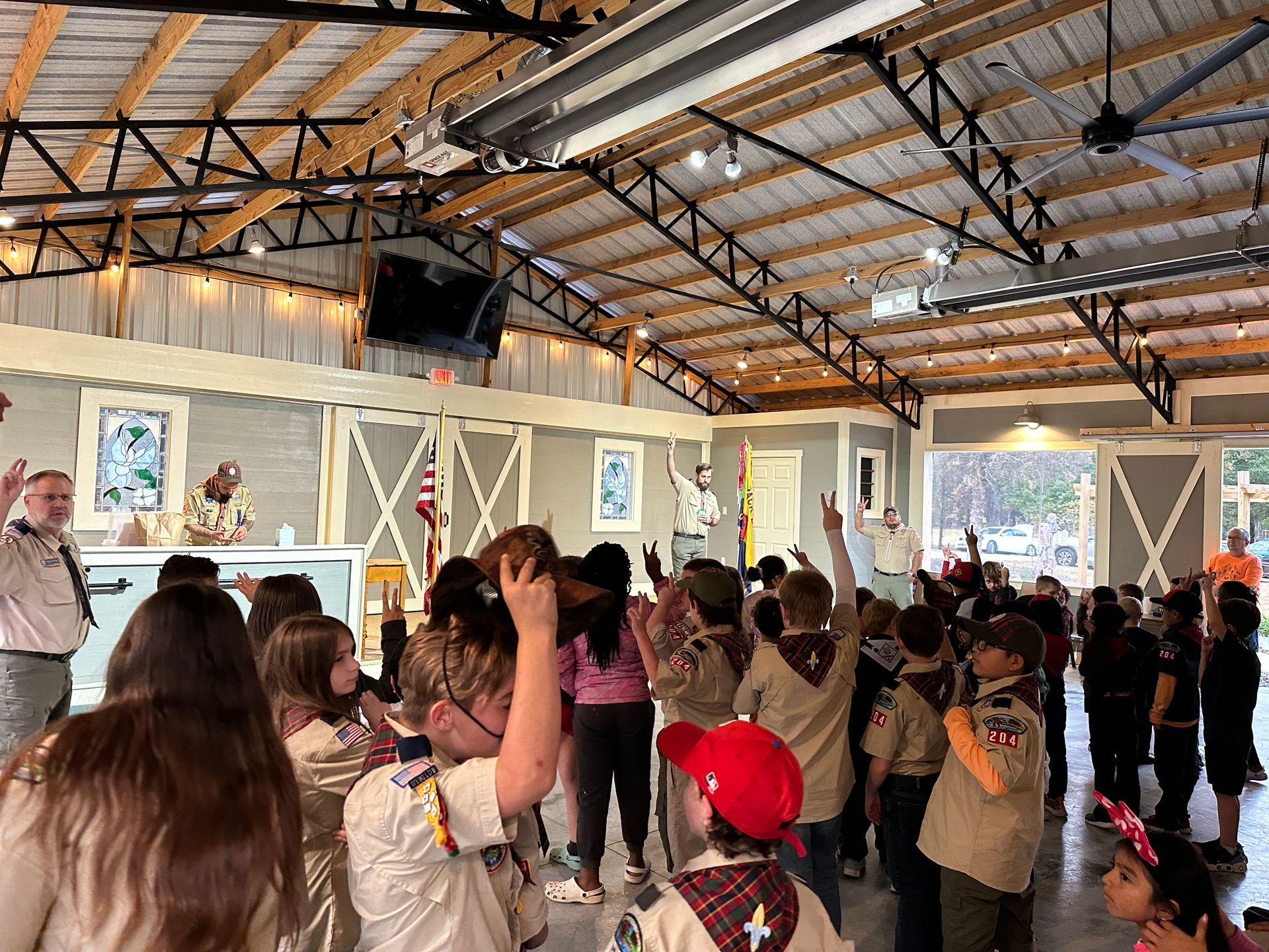 A group of boy scouts are standing in a large room raising their hands in the air.