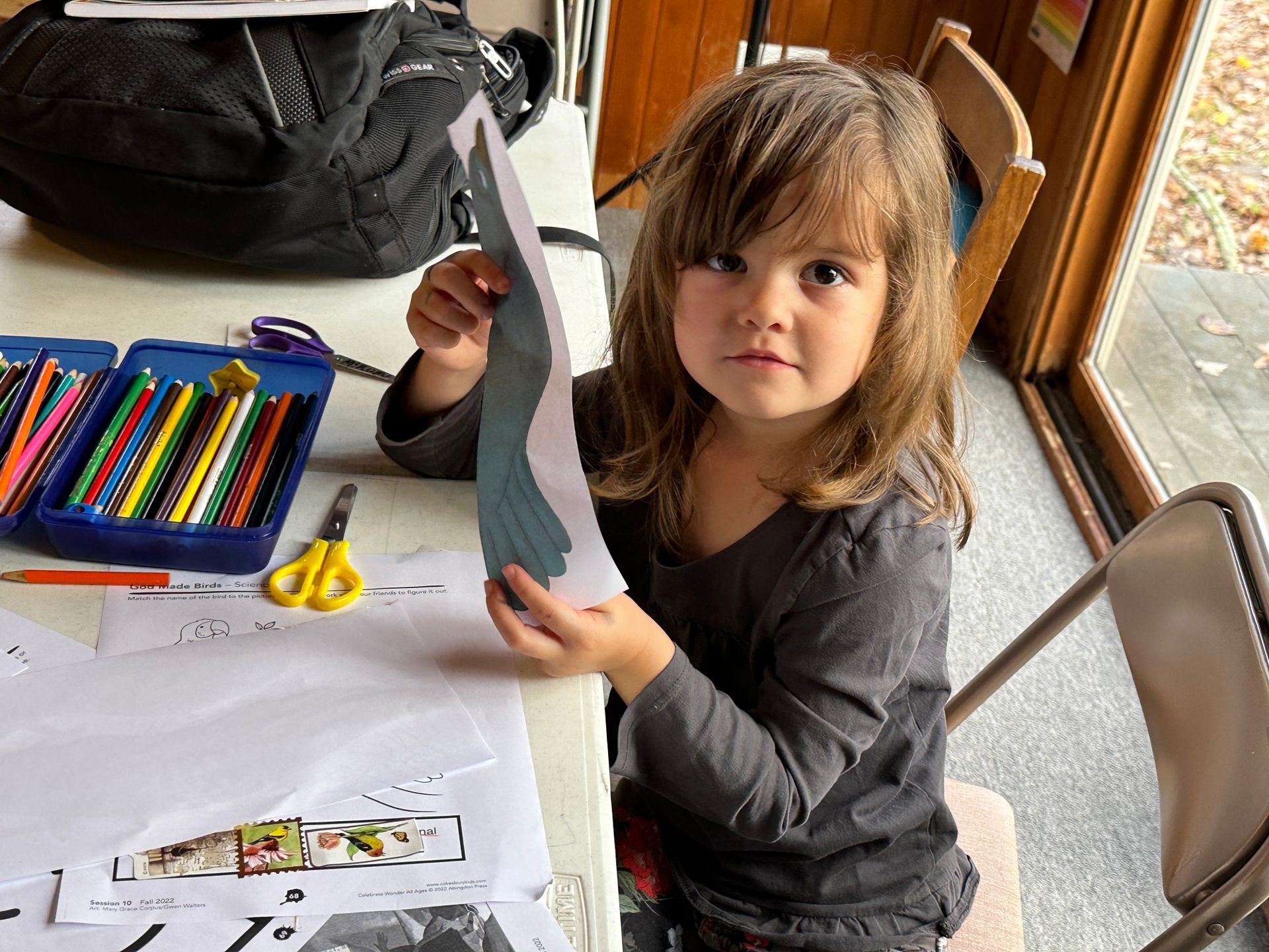 A little girl is sitting at a table holding a piece of paper.