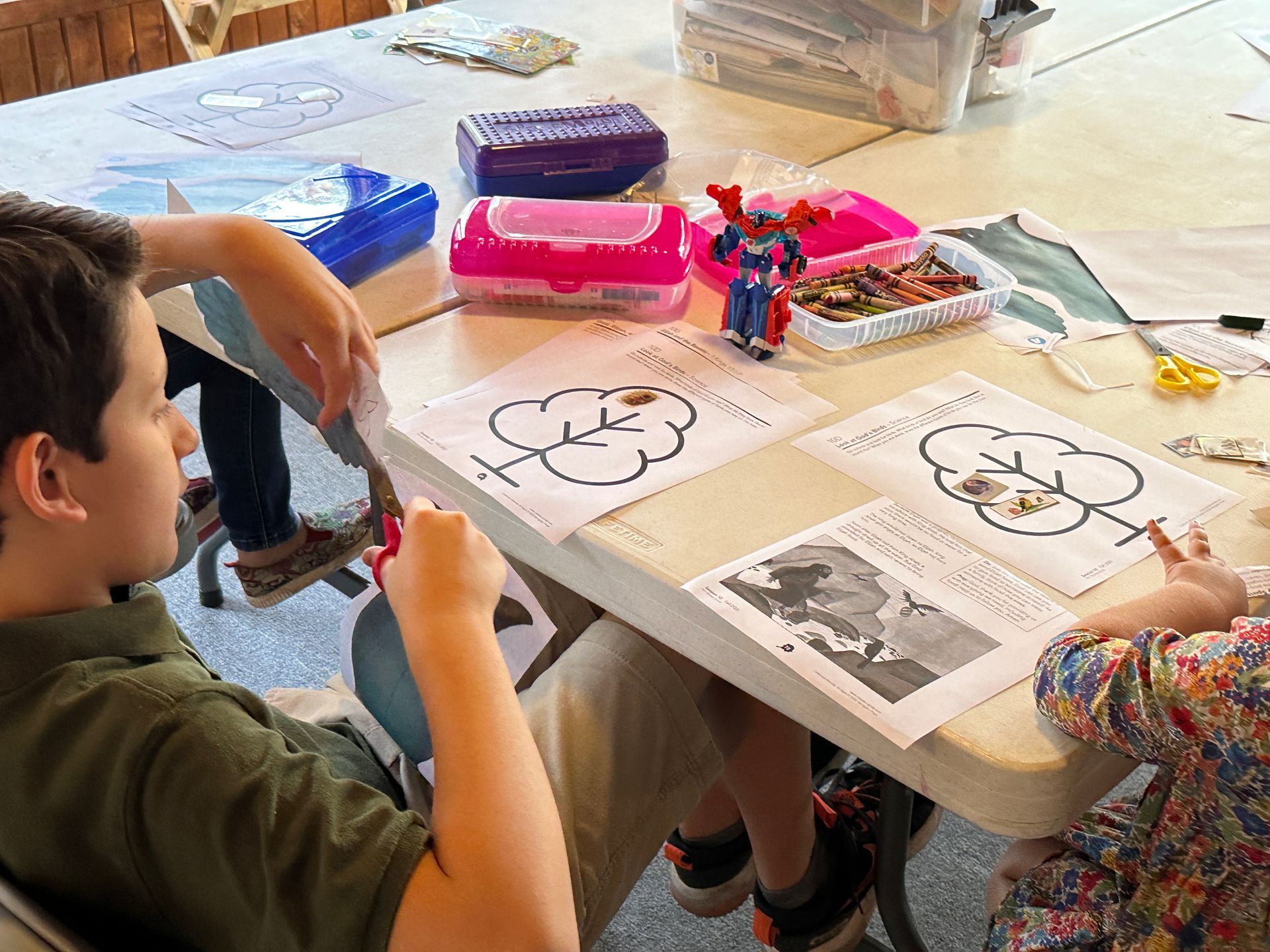 A boy and a girl are sitting at a table cutting paper with scissors.