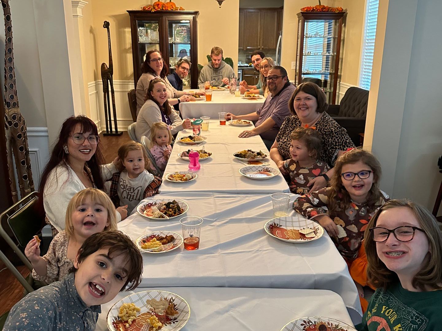 A large family is sitting at a long table with plates of food for a Friends-giving meal