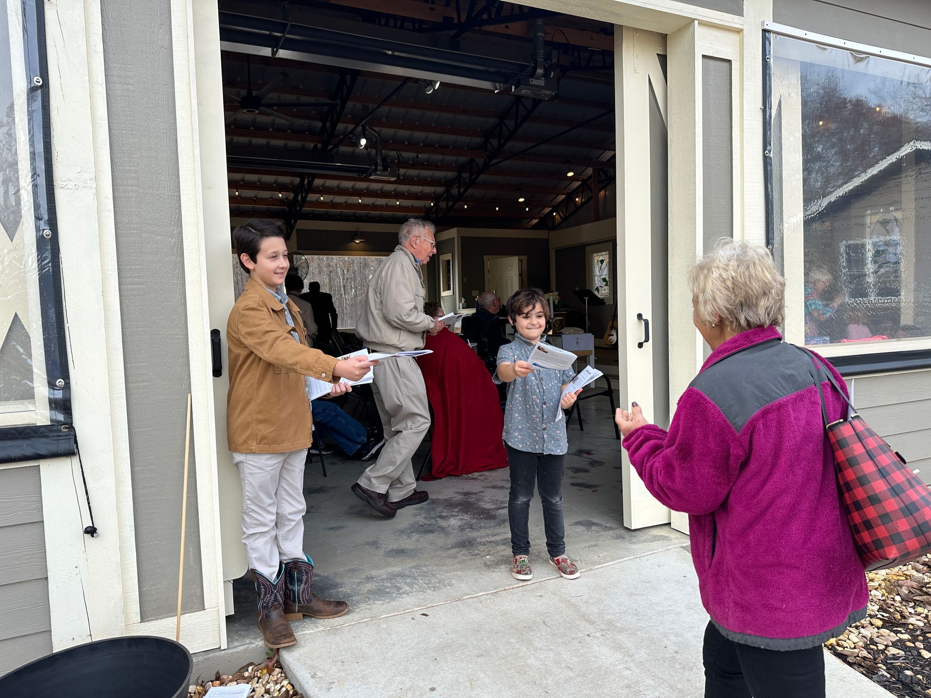 A group of people are standing outside of a pavilion handing out worship bulletins