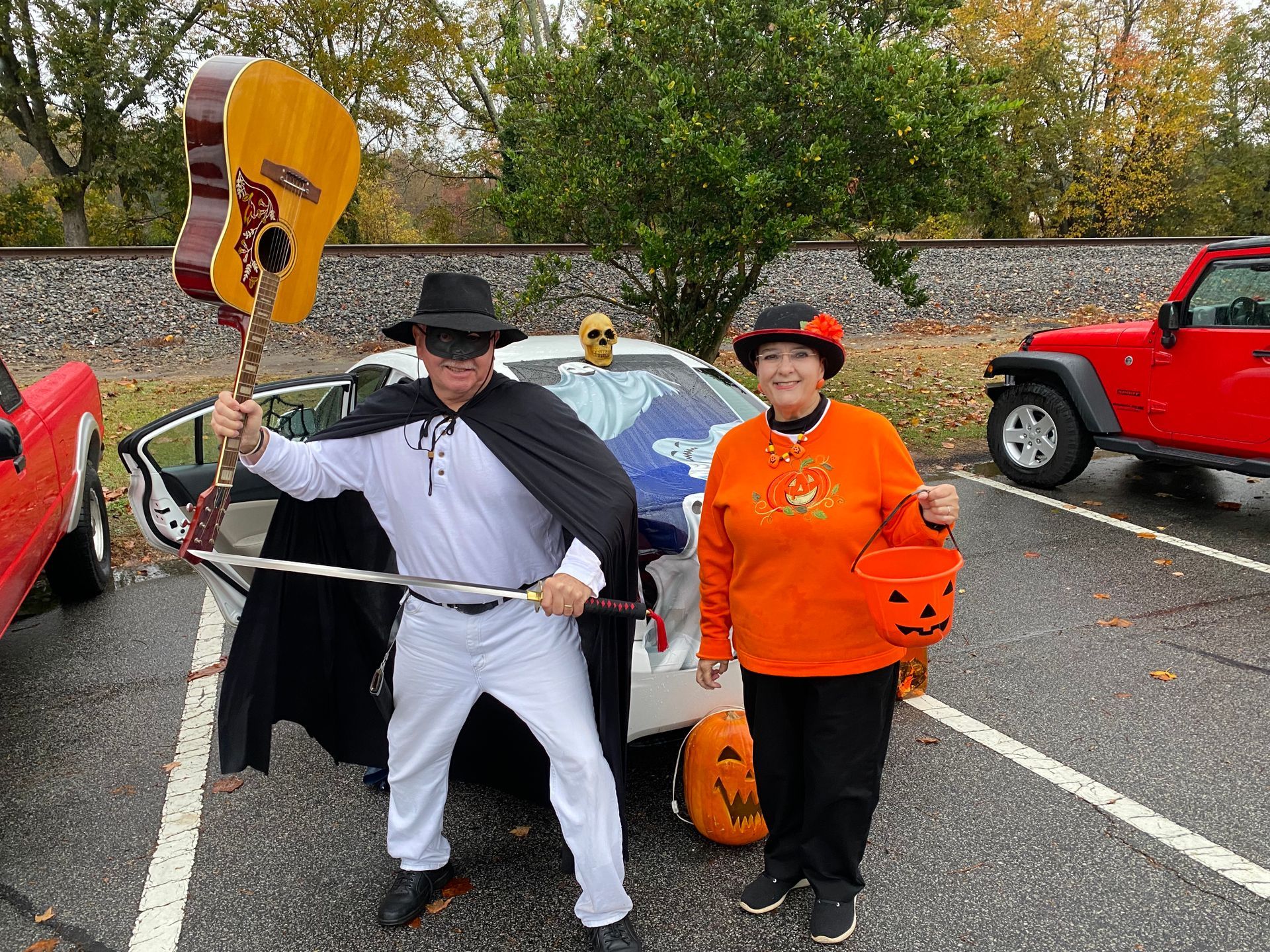 A man and a woman in halloween costumes are standing next to each other in a parking lot for Trunk or Treat