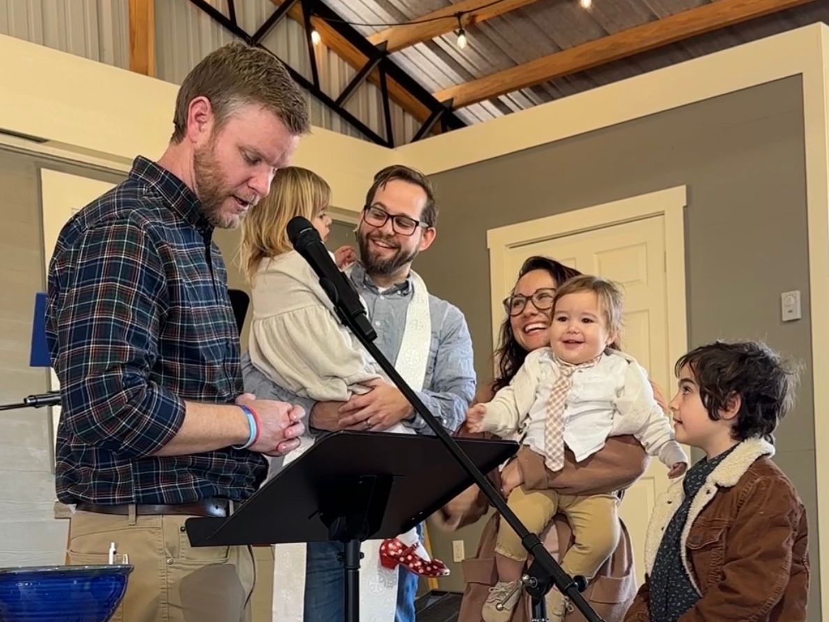 A pastor baptizing a child while family watches