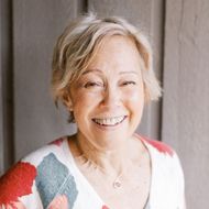 A woman wearing a floral sweater and a necklace is smiling for the camera.