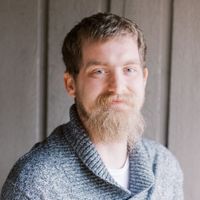 A man with a beard and a gray sweater is smiling for the camera.