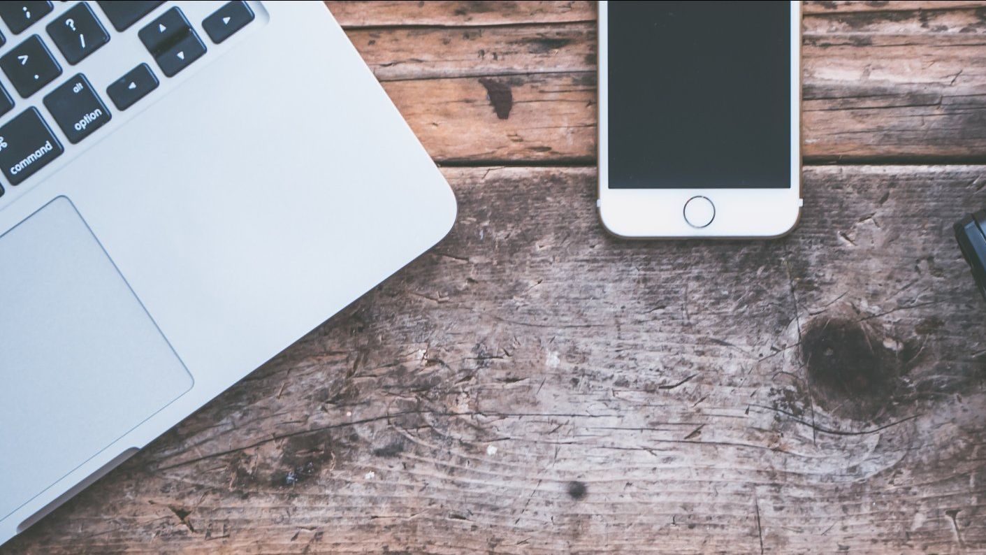 A laptop and a cell phone are on a wooden table.
