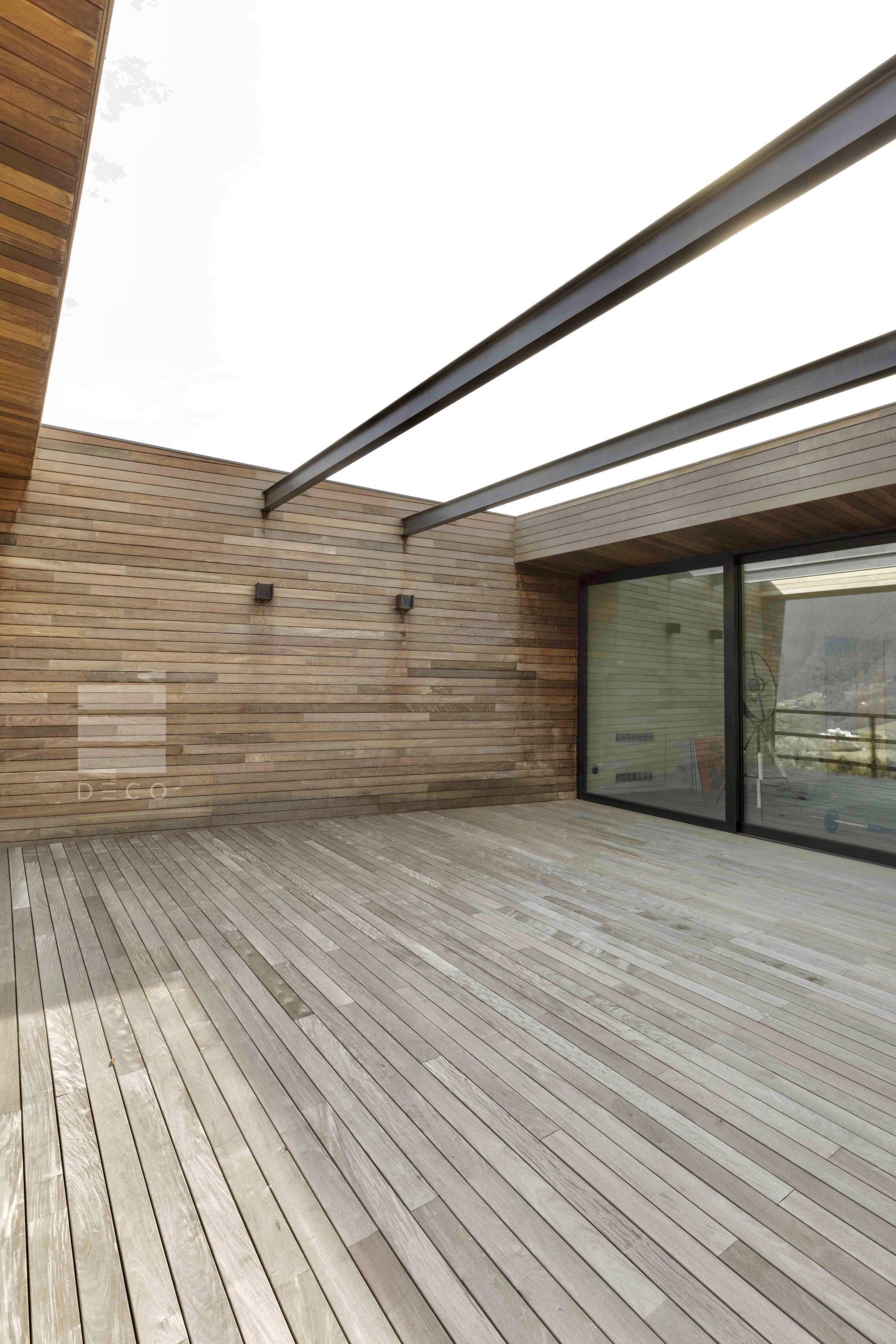 Terrazza e pareti in legno con porta in vetro e travi metalliche soprastanti.
