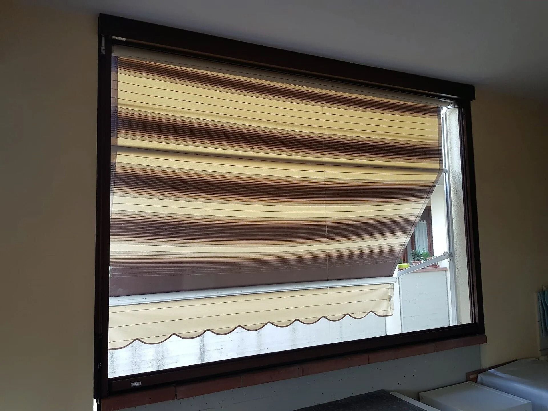 Finestra con cornice marrone e tenda a strisce color marrone chiaro e marrone.