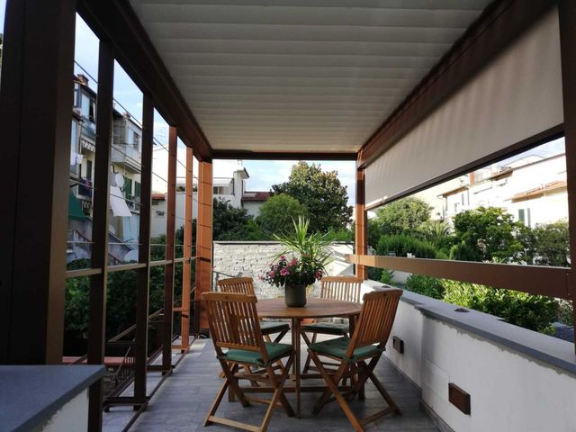 Patio esterno con mobili in legno, con vista su alberi ed edifici.