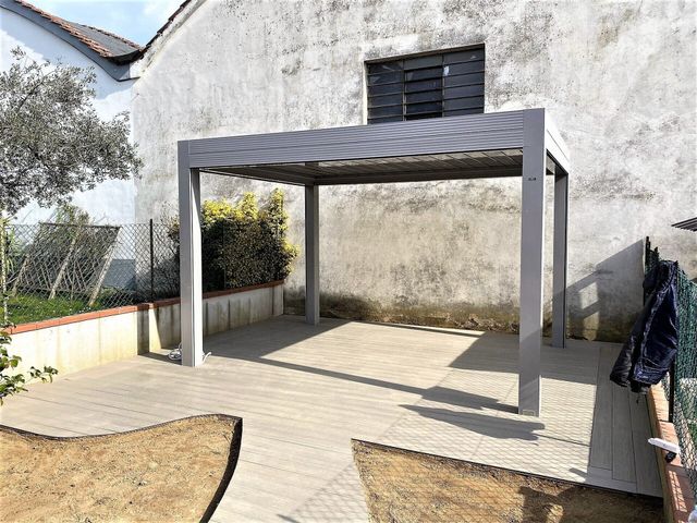 Pergola in metallo grigio su un patio in cemento di fronte a un muro bianco usurato.