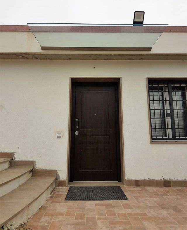 Vista esterna di un edificio con una porta marrone scuro, una finestra con le sbarre e gradini