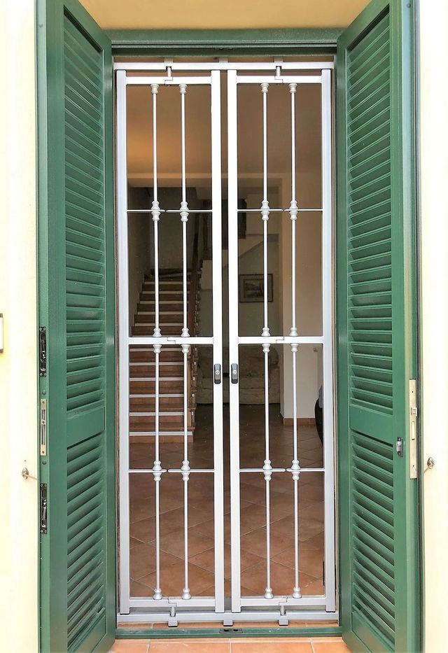 Le persiane verdi incorniciano una porta dotata di rete di sicurezza; è visibile la scala interna.