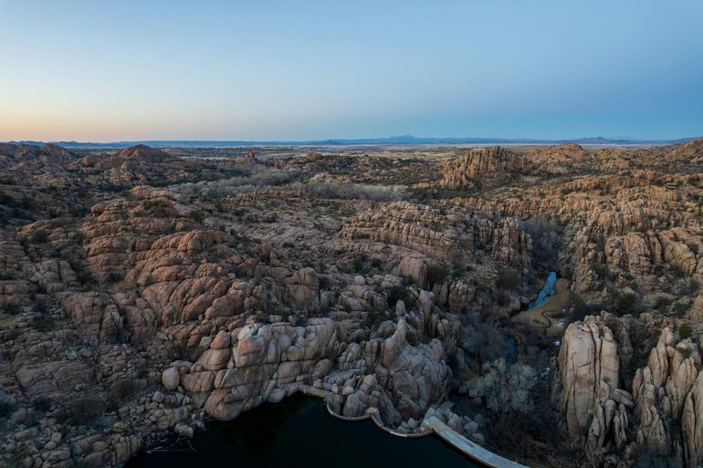 Rocky coastal cliffs at dusk with calm blue water and a distant horizon