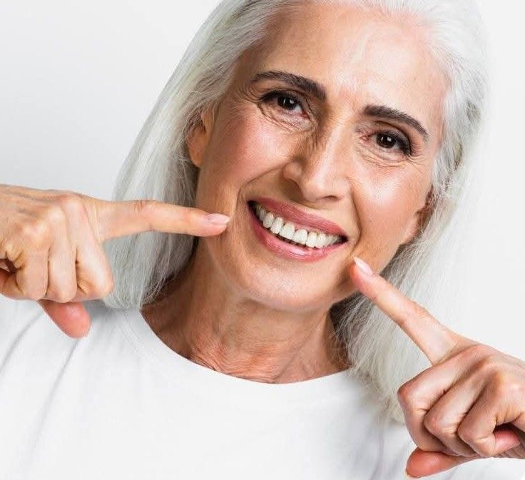 Un dentista, con indosso mascherina e guanti, tiene in mano un modellino dentale per spiegare una procedura a un paziente in uno studio medico.