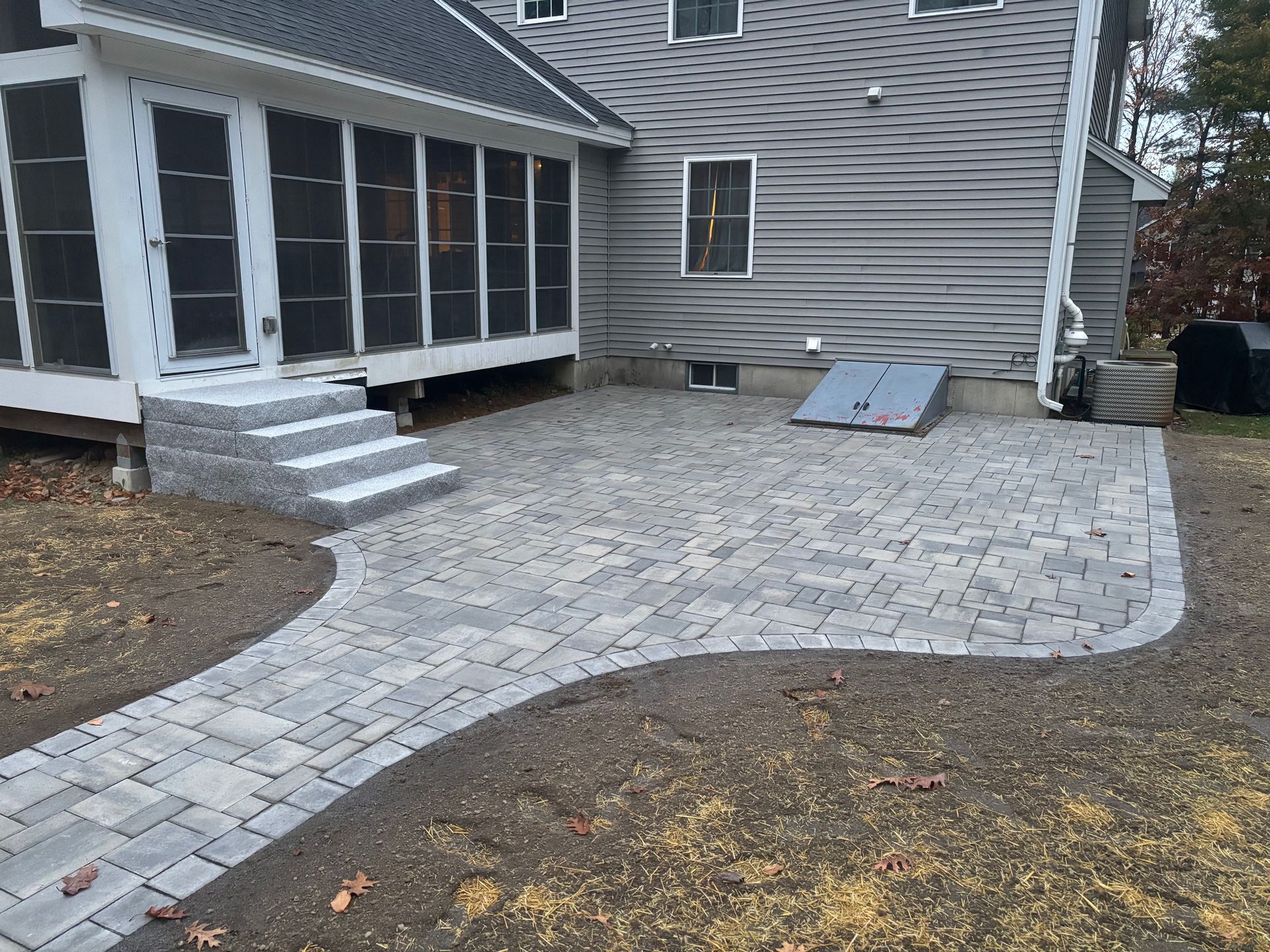 Brick patio and walkway with steps leading to a screened porch on the side of a house.