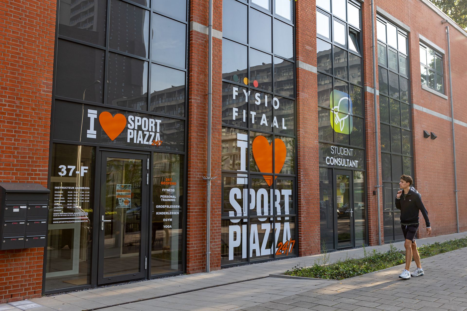 Een man staat voor een gebouw met de tekst 'Ik hou van sportpiazza'.