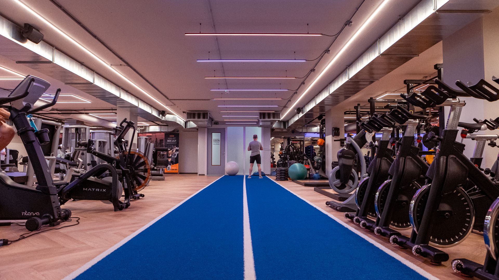 Een man staat op een blauwe baan in een sportschool.