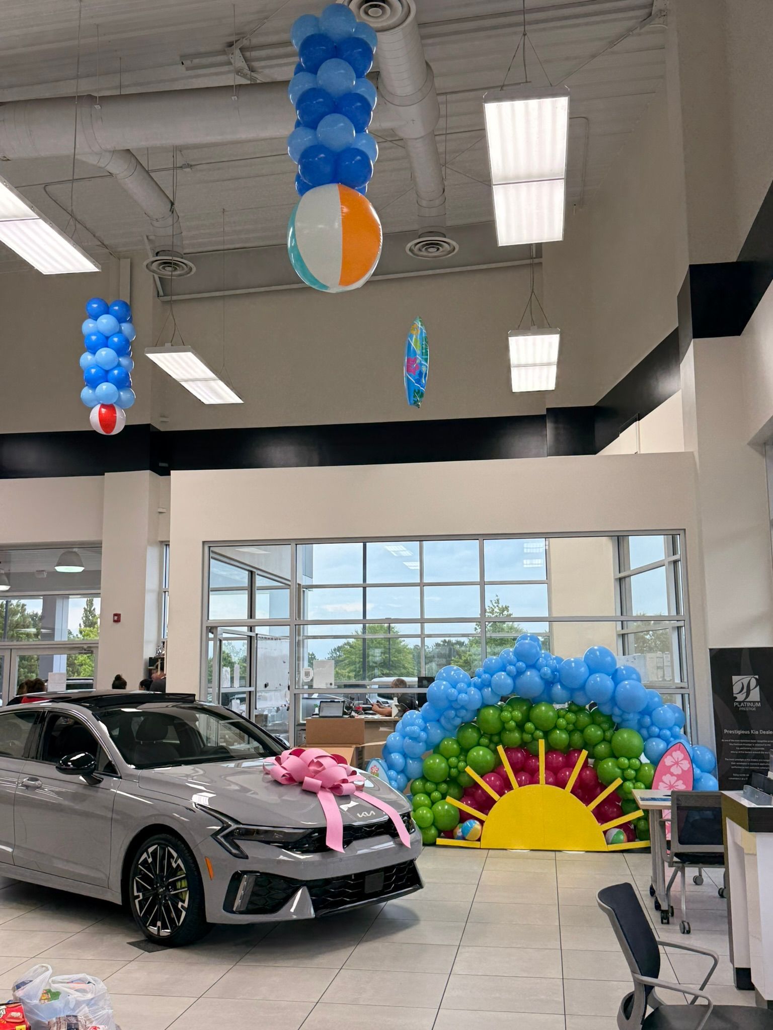 Car showroom decorated with blue balloon columns, rainbow arch, and a silver car with a pink bow.