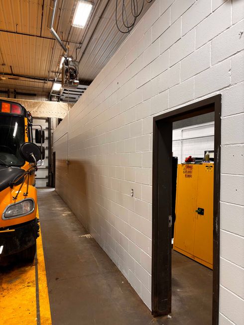 Couloir étroit de garage jouxtant un véhicule orange, avec un mur de briques blanches et une petite porte donnant sur une pièce jaune.