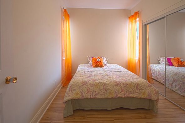 Petite chambre avec un lit simple, linge de lit à fleurs, rideaux orange et portes de placard à miroir