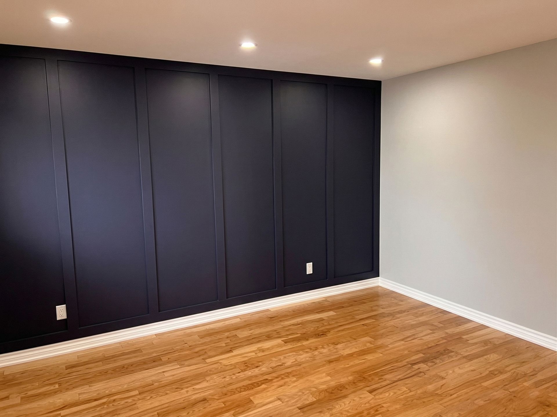 Pièce vide avec placards intégrés bleu foncé, murs gris et parquet