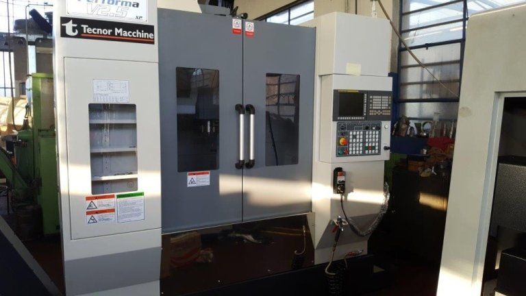 Fresatrice CNC in un'officina, bianca e grigia, con pannello di controllo e sportelli chiusi.
