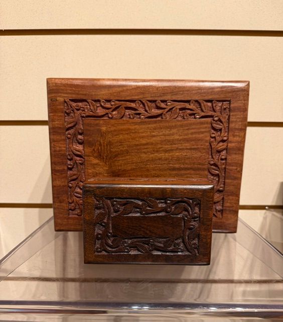 Two carved wooden decorative plaques, one large and one small, displayed on a clear shelf.