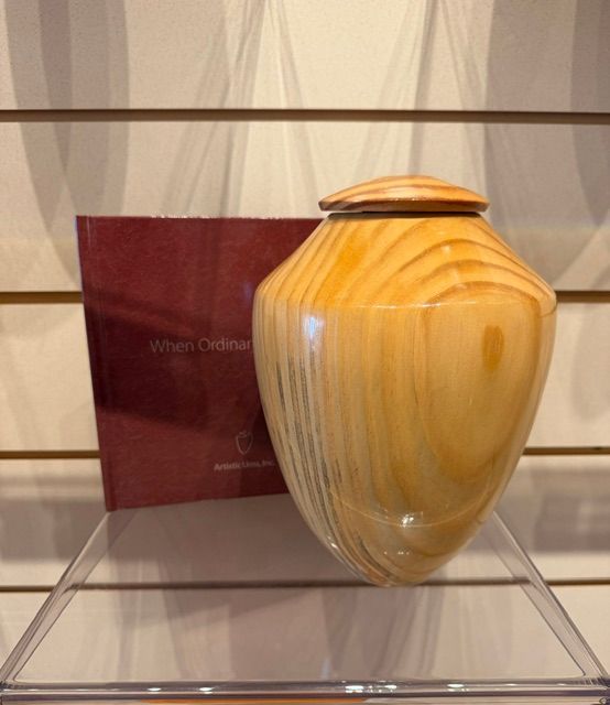 Amber and cream ceramic urn with lid on a shelf beside a maroon plaque