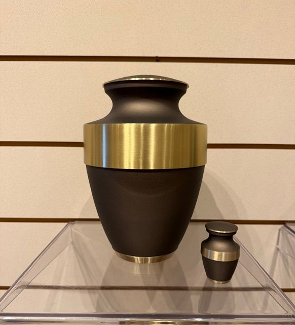 Black urn with gold band on a clear display stand, with a small matching urn beside it.