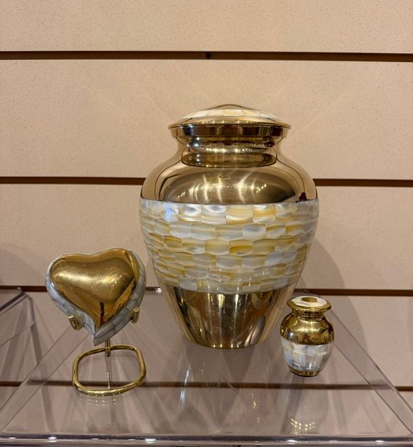 Gold and white urn centerpiece with a heart-shaped ornament and small matching vase on a display shelf