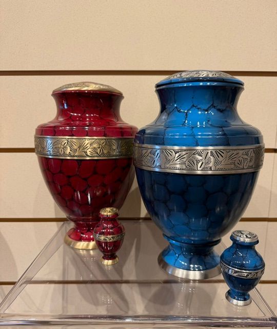 Two ornate blue and red urns with silver bands, each paired with a small matching keepsake urn on a shelf.