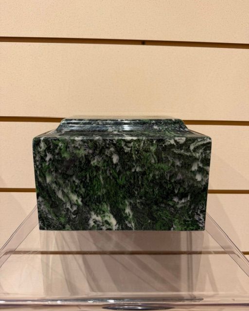 Dark green marbled rectangular box on a clear display stand against a beige wall with horizontal lines